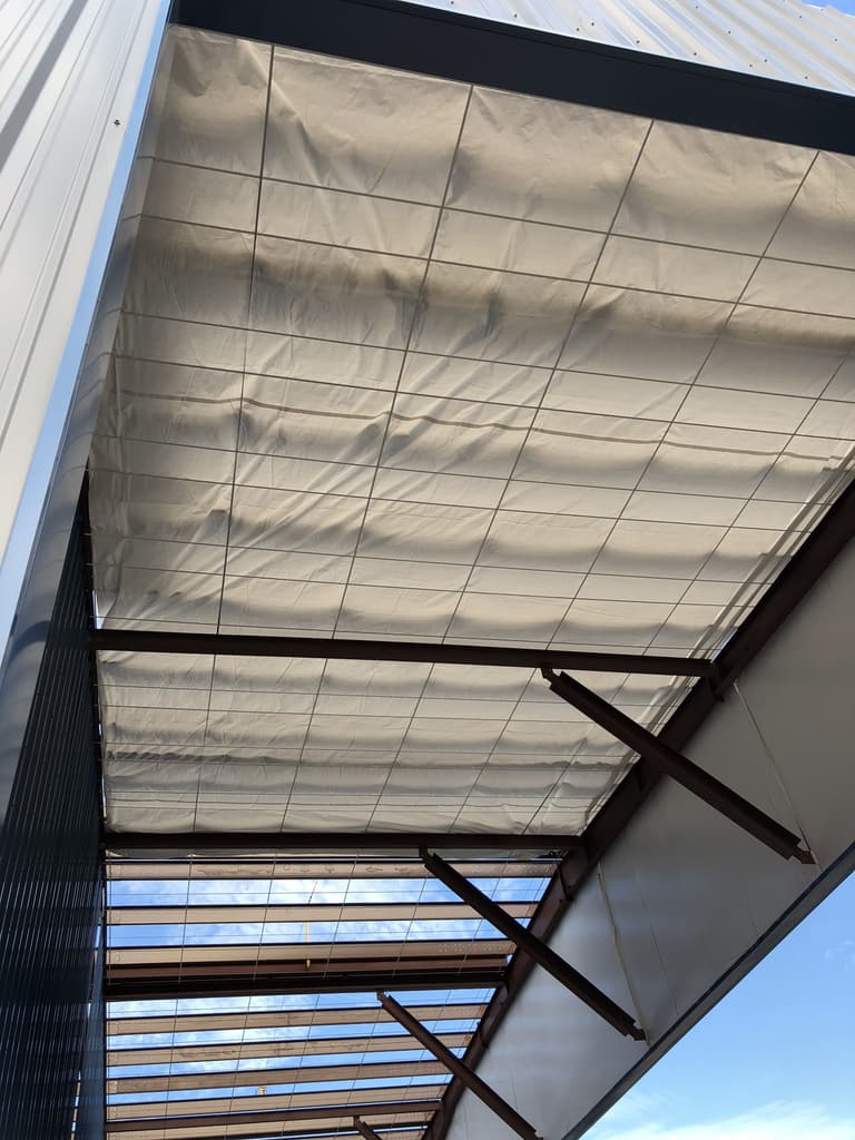 Underside of a steel canopy overhang showing roof insulation, purlins and angled steel braces against a blue sky
