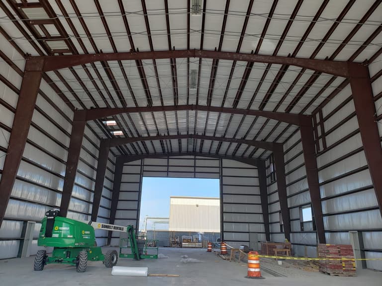Interior of an insulated steel building with red-iron rigid frames and a large open endwall door
