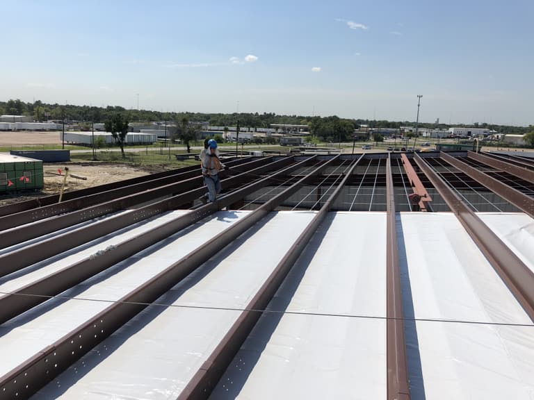 Crew member on a steel roof with red purlins and white insulation being rolled out between them