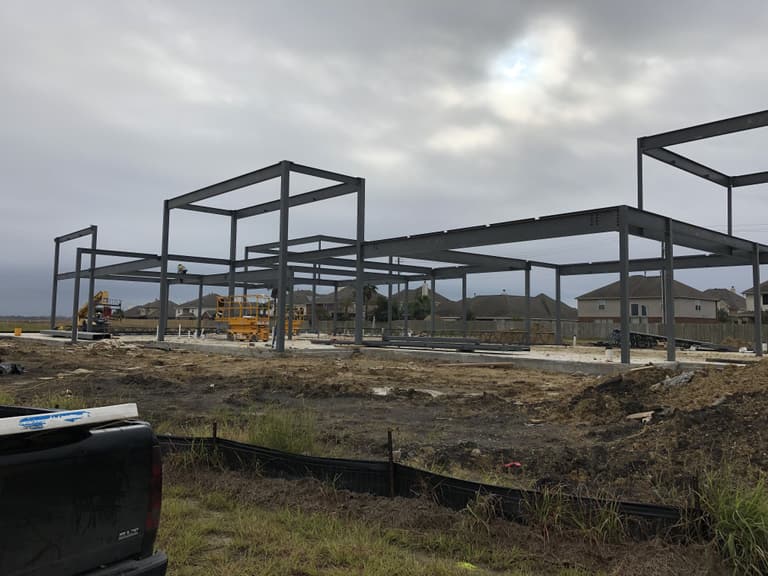 Gray structural steel columns and beams standing on a concrete slab at a new construction site under an overcast sky